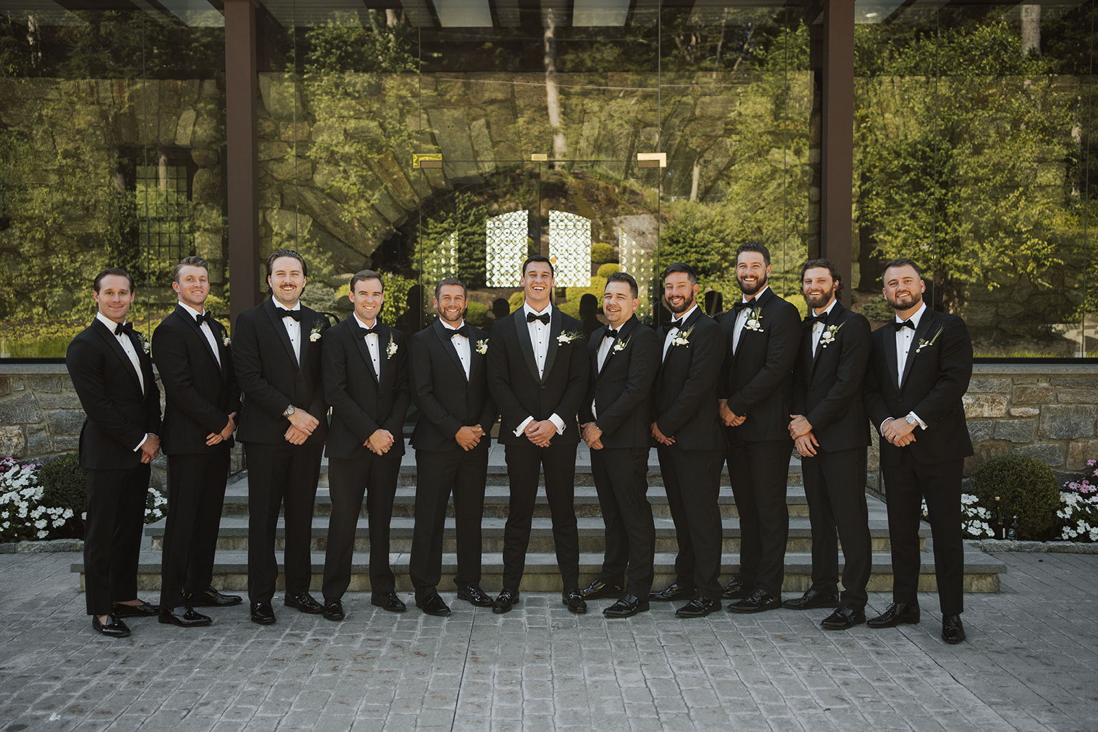 Groom and groomsmen posing in a line in front of the glass windows of Le Chateau.